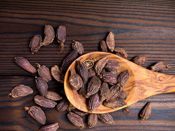 Black amomum pods in the wooden spoon on the dark wooden textured planks