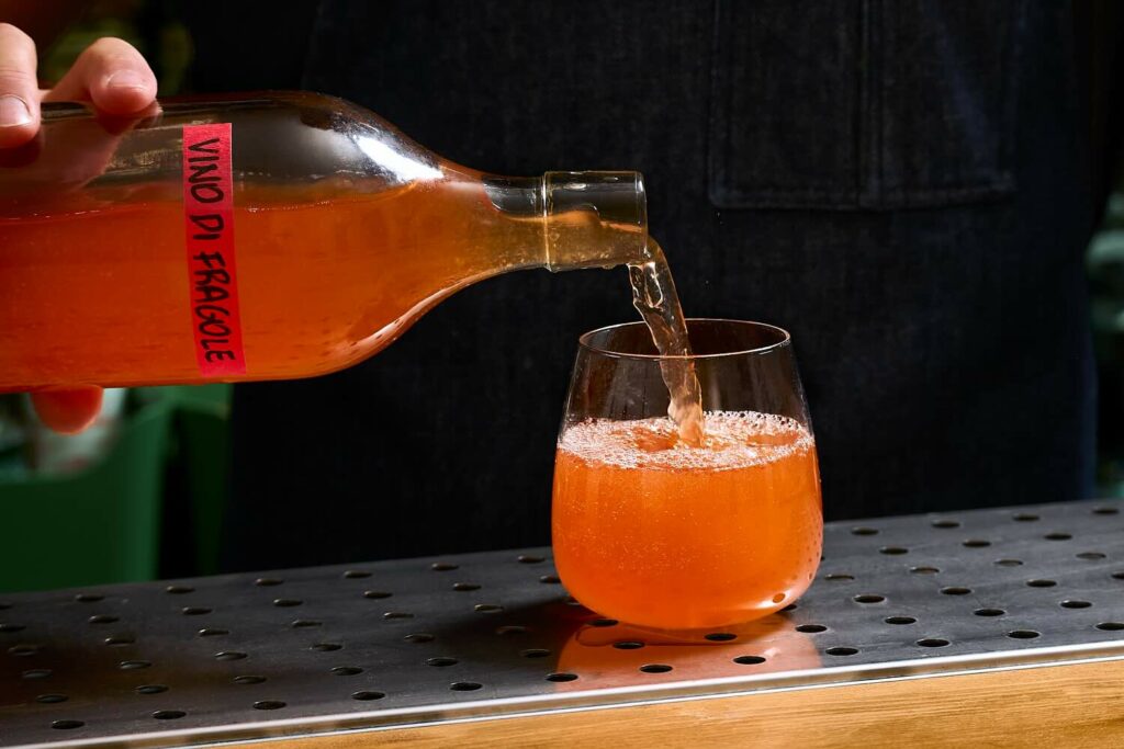 Un barman che versa in un bicchiere dalla forma tondeggiante il Vino di Fragole.