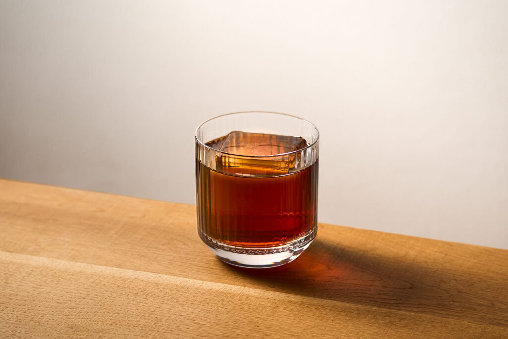 su un tavolo in legno il cocktail black russian preparato con Vodka e liquore Il cocktail è servito in un tumbler basso rigato ed è servito con chunk di ghiaccio